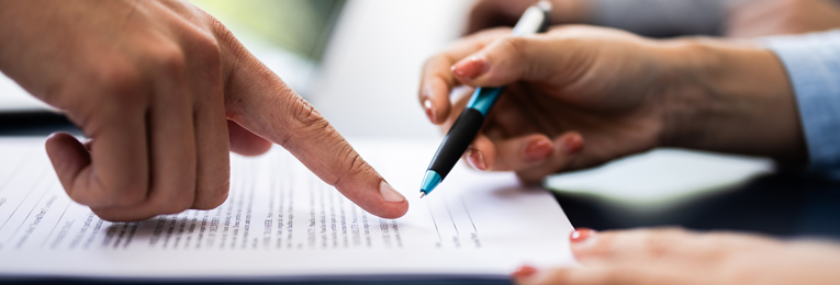 A hand is seen filling out a form while another person's hand points at the document.